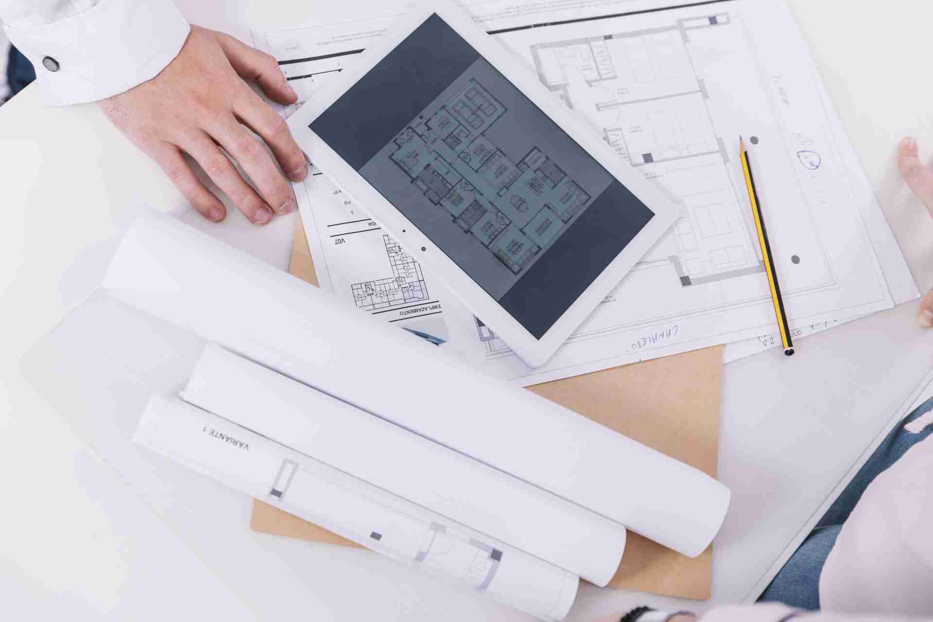 person with laptop and blueprints signifying the use of architectural drafting for project.